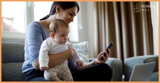 Mother holding an infant while looking at her phone